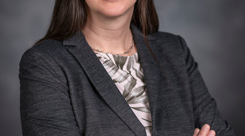 Portrait of Ann Wehman sitting with arms raised against a blue background