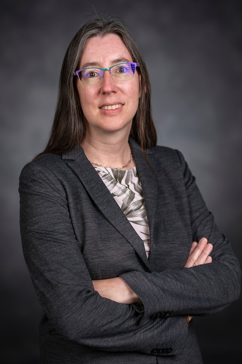 Portrait of Ann Wehman sitting with arms raised against a blue background